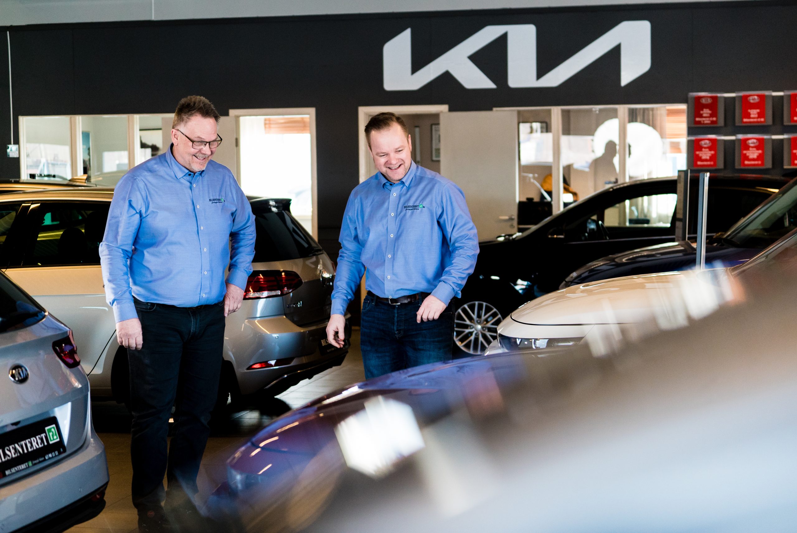 2 menn i blå shorter som smiler å ser på biler